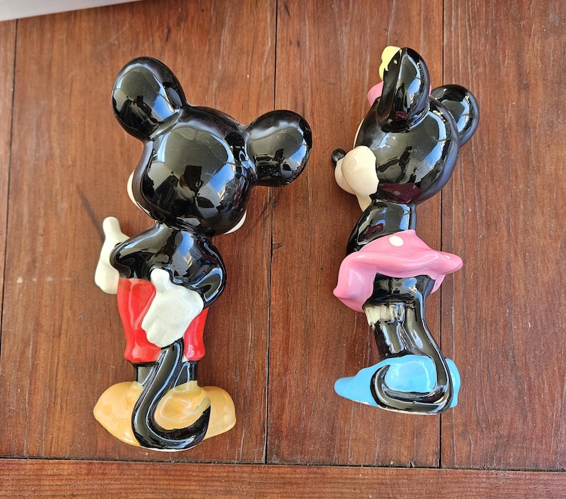 May include: A black and white ceramic figurine of Mickey Mouse wearing red shorts and black shoes.  A black and white ceramic figurine of Minnie Mouse wearing a pink dress and blue shoes.