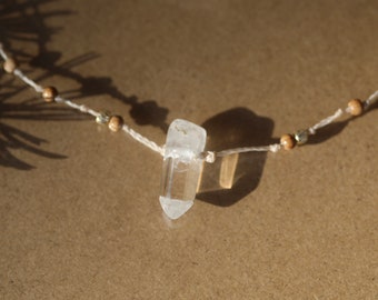 May include: A clear quartz crystal pendant on a simple string necklace with brown wooden beads.
