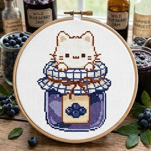Pode incluir: Um bastidor de bordado em ponto cruz com um gato branco espreitando de um frasco de geleia de mirtilo. O frasco é roxo com uma tampa xadrez azul e branca. O bordado está num bastidor de madeira.