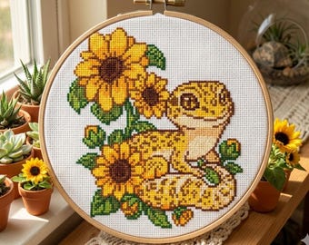 May include: Cross-stitch embroidery in a wooden hoop features a yellow gecko surrounded by sunflowers. The gecko has a detailed pattern in shades of yellow and brown. The sunflowers have yellow petals and brown centers, with green leaves.