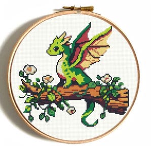May include: A green and yellow dragon with red wings sits on a brown branch with green leaves and white flowers. The dragon has a long tail and is looking to the left.