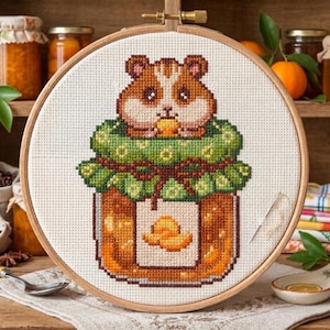 May include: Cross-stitch embroidery of a hamster inside a jar of jam. The hamster is brown and white, and the jam jar is orange and brown. The embroidery is set in a wooden hoop, with a needle and thread visible.