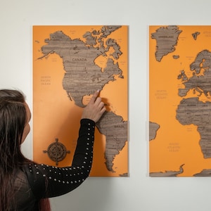 May include: A three-panel wooden world map with a light orange background. Each panel features a different continent. The map is made of wood and has a raised, textured design. The map is mounted on a white wall.
