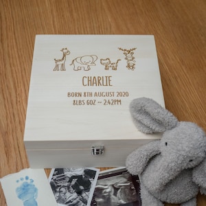 May include: A white wooden keepsake box with a hinged lid. The box is engraved with a giraffe, elephant, cat, and monkey, along with the name "Charlie", the date "Born 8th August 2020", and the weight "8lbs 6oz ~ 2:42PM". A gray elephant stuffed animal is sitting on the table next to the box.