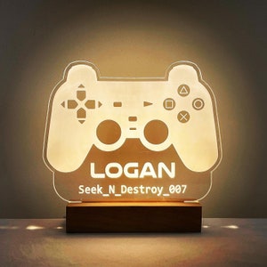 May include: A white illuminated acrylic gaming controller night light with the name "LOGAN" and the gamertag "Seek_N_Destroy_007" printed below. The light is sitting on a wooden base.
