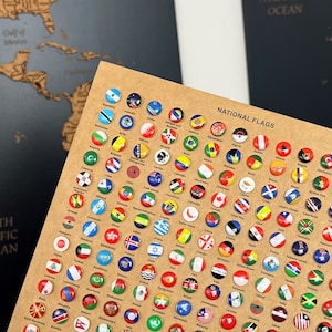 Könnte beinhalten: Nahaufnahme einer braunen Karte mit dem Aufdruck "National Flags". Die Karte ist mit kleinen, runden, bunten Aufklebern bedeckt, die die Flaggen verschiedener Länder darstellen.