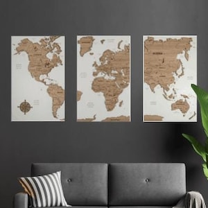 Peut inclure: Trois cartes du monde en liège dans un cadre blanc, chaque carte représente un continent différent. Les cartes sont accrochées à un mur gris foncé.