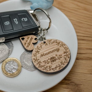 May include: A white ceramic dish with a car key, a blue bird figurine, and a wooden keychain with the words "Mummy" and "To the best of" on it.