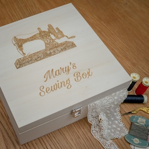 May include: A white wooden sewing box with a hinged lid. The lid has an engraved image of a sewing machine and the text "Mary's Sewing Box".