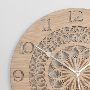 May include: A wooden clock with a decorative, laser-cut design in the center. The clock face has Roman numerals and a silver-colored hour and minute hand.