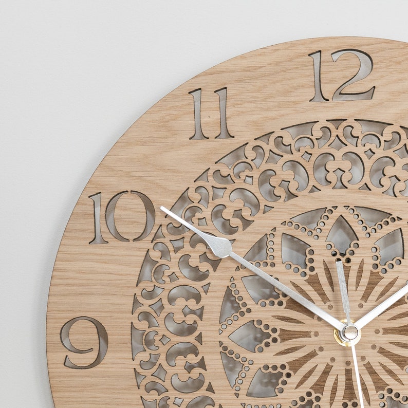 May include: A wooden clock with a decorative, laser-cut design in the center. The clock face has Roman numerals and a silver-colored hour and minute hand.
