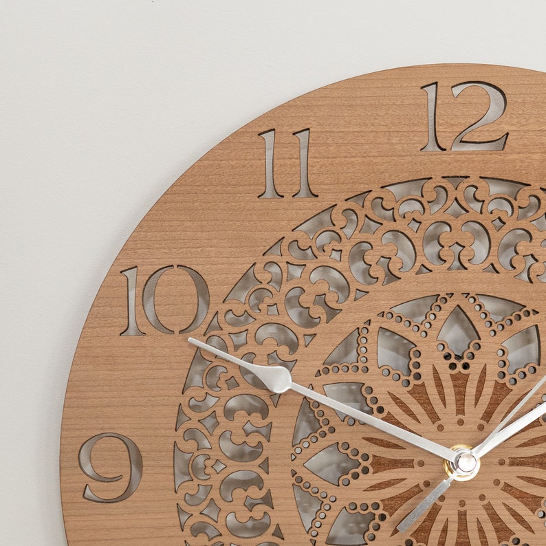 May include: A wooden clock with a decorative, laser-cut design. The clock face features Roman numerals and a silver-colored hour and minute hand.