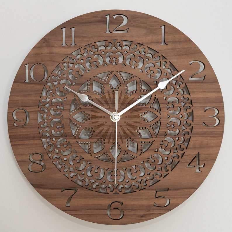 May include: A brown wooden clock with a decorative mandala design and silver hands. The clock face has Roman numerals for the hours and Arabic numerals for the minutes.
