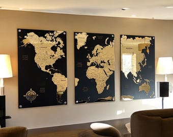 May include: Three black framed world maps with gold foil accents. The maps are mounted on a wall in a living room setting.