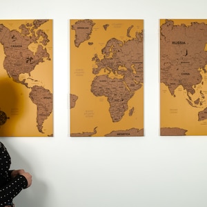 May include: Three cork world maps mounted on a wall. The maps are divided into three sections: North and South America, Europe, Africa, and Asia, Australia. Each map has a yellow background and black outlines of the continents and countries.
