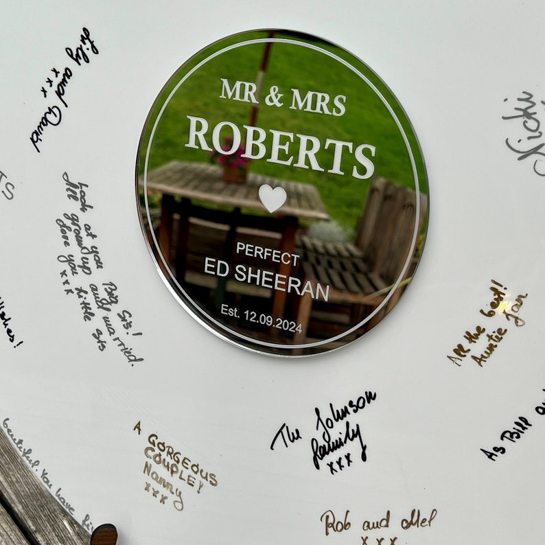 Pode incluir: Uma placa de casamento redonda e espelhada com o texto "MR & MRS ROBERTS" e "PERFECT ED SHEERAN" em branco. A data "Est. 12.09.2024" tamb&eacute;m est&aacute; inclu&iacute;da. A placa &eacute; rodeada por mensagens manuscritas.