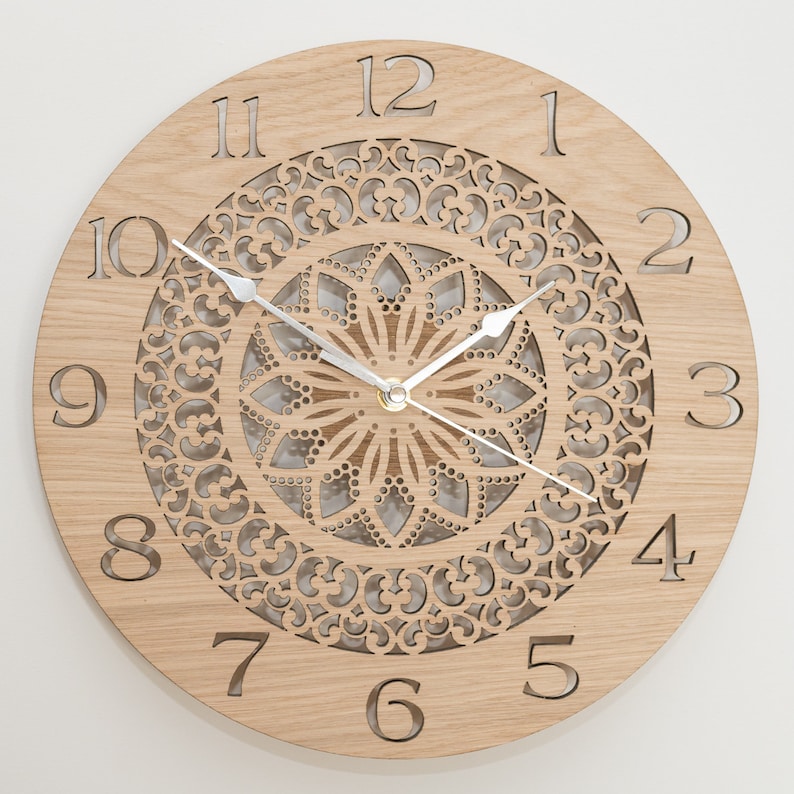 May include: A wooden wall clock with a decorative, laser-cut mandala design. The clock face features Roman numerals and a silver-toned hour and minute hand.
