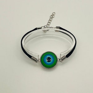 Puede incluir: Un brazalete de cordón negro con una cadena plateada y un dije de ojo turco azul y verde.