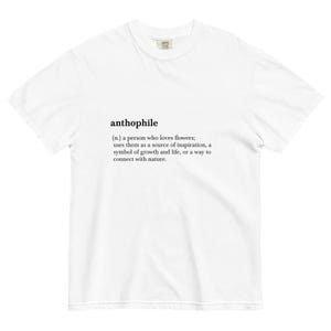 May include: White t-shirt with the word "anthophile" printed on the front. The definition of the word is printed below: "(n.) a person who loves flowers; uses them as a source of inspiration, a symbol of growth and life, or a way to connect with nature."