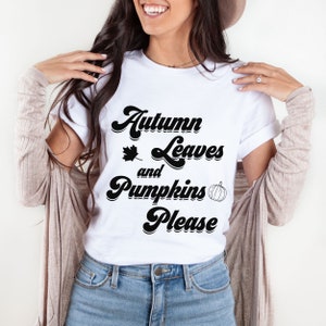 May include: White t-shirt with a black graphic that says "Autumn Leaves and Pumpkins Please" in a retro font. The graphic also includes a small leaf and a pumpkin.