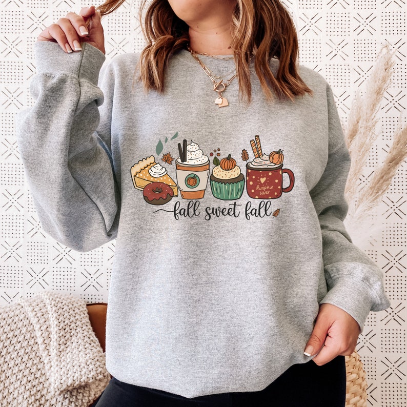 May include: Gray sweatshirt with a graphic of fall-themed treats, including a pumpkin spice latte, a cupcake, a slice of pie, a donut, and a mug that says "Pumpkin Spice Latte". The text "fall sweet fall" is printed below the graphic.