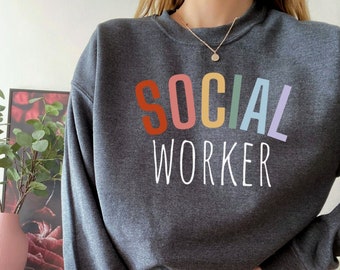 May include: A dark gray sweatshirt with the text "SOCIAL WORKER" in white. The word "SOCIAL" is in rainbow colors.