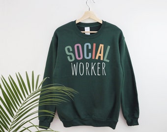May include: A dark green sweatshirt with the text "SOCIAL WORKER" in rainbow colors. The text is in a stylized font with each letter in a different color.