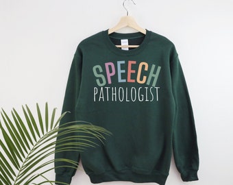 May include: A dark green sweatshirt with the text "SPEECH PATHOLOGIST" in rainbow colors.
