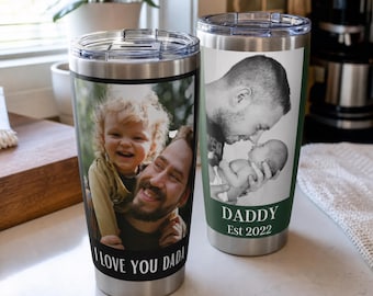 May include: Two stainless steel tumblers with clear plastic lids. The left tumbler features a color photo of a child and adult with the text I LOVE YOU DADA. The right tumbler features a black and white photo of an adult and infant with DADDY Est 2022.