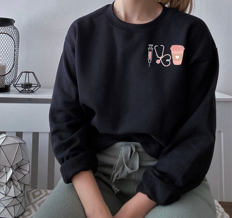 May include: Black sweatshirt with a pink graphic of a syringe, stethoscope, heart, and coffee cup.