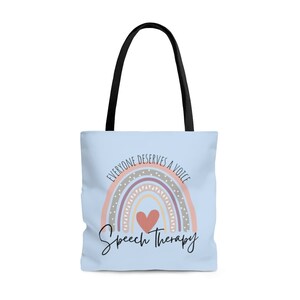 May include: A light blue tote bag with black handles. The bag features a rainbow with a heart in the center and the text "Everyone deserves a voice" above the rainbow and "Speech Therapy" below the rainbow.