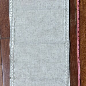 May include: Beige linen table runner with hand-painted roses in pink and yellow. The runner is approximately 48 inches long and features a decorative border. The roses are set against a green background.