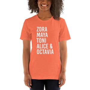 May include: A coral-colored t-shirt with the names Zora, Maya, Toni, Alice & Octavia printed in white.