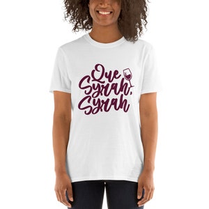 Puede incluir: Camiseta blanca con la frase "Que Syrah, Syrah" en escritura burdeos, acompa&ntilde;ada de un gr&aacute;fico de copa de vino. La camiseta es de cuello redondo y manga corta.
