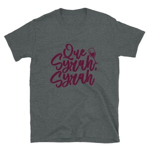 Puede incluir: Camiseta gris oscuro con la frase "Que Syrah, Syrah" en borgo&ntilde;a, en fuente cursiva, y un dibujo de copa de vino. La camiseta est&aacute; hecha de un material suave.