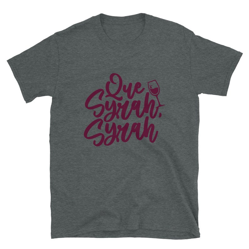 Puede incluir: Camiseta gris oscuro con la frase "Que Syrah, Syrah" en borgo&ntilde;a, en fuente cursiva, y un dibujo de copa de vino. La camiseta est&aacute; hecha de un material suave.