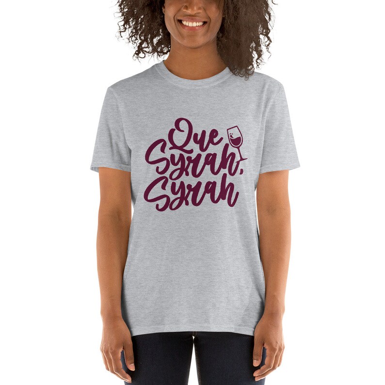 Puede incluir: Camiseta gris claro con la frase "Que Syrah, Syrah" en borgo&ntilde;a, en una fuente de escritura. Un gr&aacute;fico de copa de vino est&aacute; al lado del texto. La camiseta es de cuello redondo y manga corta.