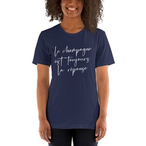 May include: Navy blue t-shirt with the white cursive text "Le champagne est toujours la r&eacute;ponse." The shirt is a crew neck and has short sleeves. The shirt is made of a soft material.