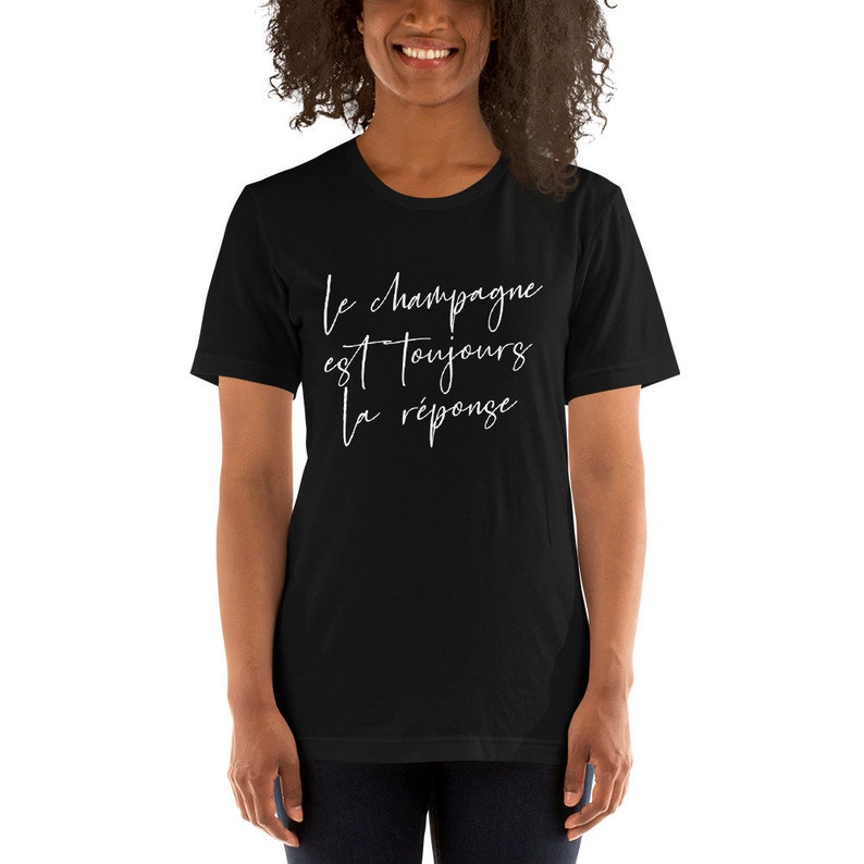 May include: Black t-shirt with the white script text "Le champagne est toujours la r&eacute;ponse." The shirt is a crew neck style and is being worn by a person.