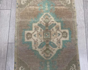 Puede incluir: Una alfombra tejida rectangular que presenta un medallón central en forma de diamante en tonos marrón apagado, beige y azul verdoso suave. El intrincado patrón geométrico incluye motivos florales simétricos y un borde con formas.