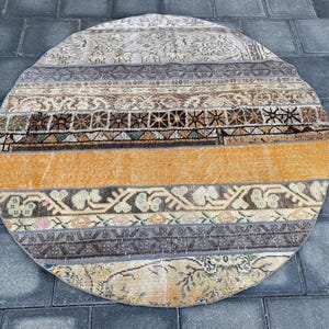 Könnte beinhalten: Ein runder, mehrfarbiger Teppich mit Patchwork-Muster. Der Teppich hat eine Vielzahl von Farben, darunter Braun, Beige, Orange und Weiß. Der Teppich ist aus gewebtem Stoff gefertigt und hat einen Fransenrand.