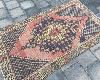 May include: A rectangular, vintage rug with a geometric design. The rug features a central pattern in shades of red, navy, and beige, with a repeating border. The rug is placed on a gray tiled surface.