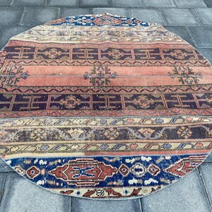 Puede incluir: Una alfombra redonda vintage con un patrón geométrico colorido en tonos rojos, azules y beige. La alfombra tiene un aspecto desgastado y descolorido, lo que aumenta su encanto.