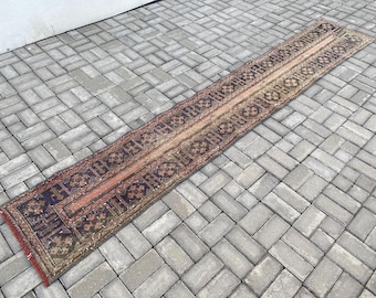 Peut inclure: Un tapis long et étroit avec un motif persan traditionnel. Le tapis est de couleur rouge, marron et crème avec des motifs géométriques complexes. Le tapis est posé sur un sol en béton gris.