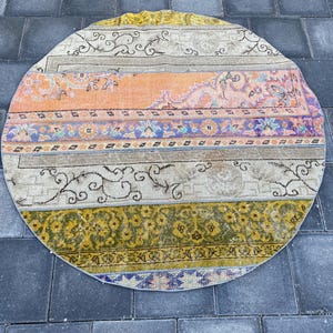 Könnte beinhalten: Ein runder, mehrfarbiger Teppich mit einem gestreiften Muster. Der Teppich hat Farbtöne von Gelb, Orange, Rosa, Lila und Weiß. Der Teppich ist aus gewebtem Stoff und hat einen Vintage-Look.