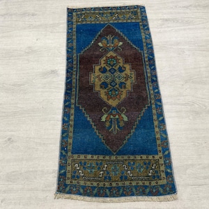May include: A rectangular area rug featuring a deep blue border and a central dark brown diamond-shaped medallion. The medallion contains intricate geometric and floral patterns in shades of gold, teal, and rust. The rug has a short fringe at both ends.