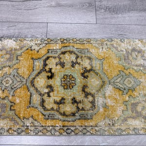 Puede incluir: Una alfombra rectangular desgastada con un dise&ntilde;o de medall&oacute;n central. La alfombra presenta una paleta de colores dorados, verde salvia y crema, con acentos marrones oscuros. El patr&oacute;n de la alfombra es un dise&ntilde;o tradicional y ornamentado.