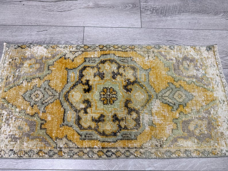 Puede incluir: Una alfombra rectangular desgastada con un dise&ntilde;o de medall&oacute;n central. La alfombra presenta una paleta de colores dorados, verde salvia y crema, con acentos marrones oscuros. El patr&oacute;n de la alfombra es un dise&ntilde;o tradicional y ornamentado.