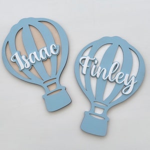 May include: Two light blue wooden hot air balloon ornaments with white names, Isaac and Finley, cut out in the centre of each balloon.