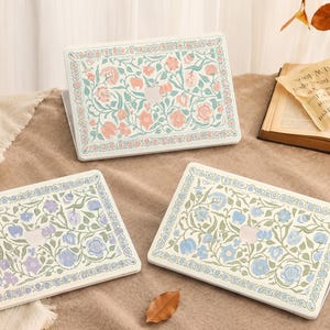 Peut inclure: Trois housses d'ordinateur portables rectangulaires ornées de motifs floraux complexes dans des tons pastel doux. Chaque housse présente une palette de couleurs unique de fleurs roses, violettes ou bleues avec un feuillage vert.
